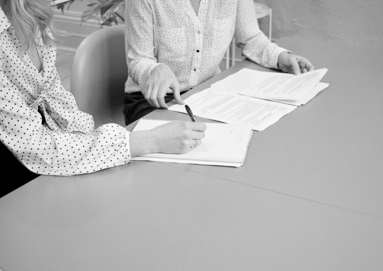 Young woman takes notes on a desk next to a colleague